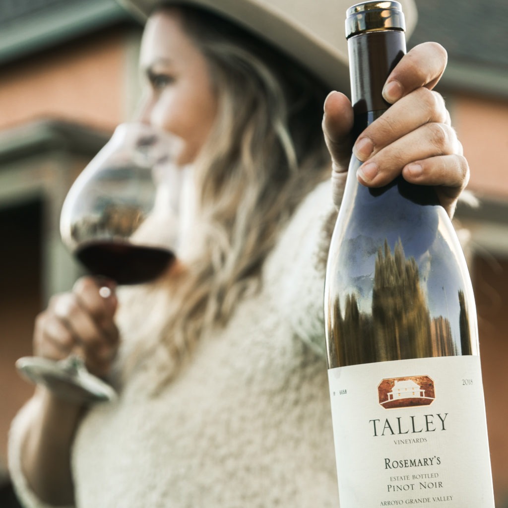 Woman holds a bottle of 2018 Rosemary's Pinot Noir by Talley Vineyards.