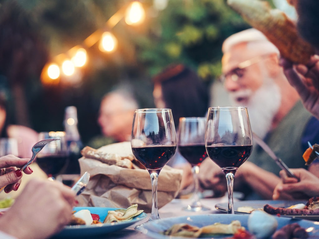Happy family eating and drinking red wine at dinner barbecue party outdoor - Mature and young people dining together on rooftop - Youth and elderly weekend lifestyle activities - Focus on wineglass
